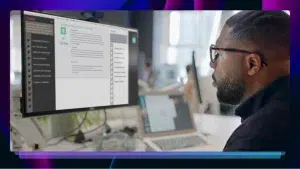 A man in glasses looks at a computer with an AI chatbot on the screen.