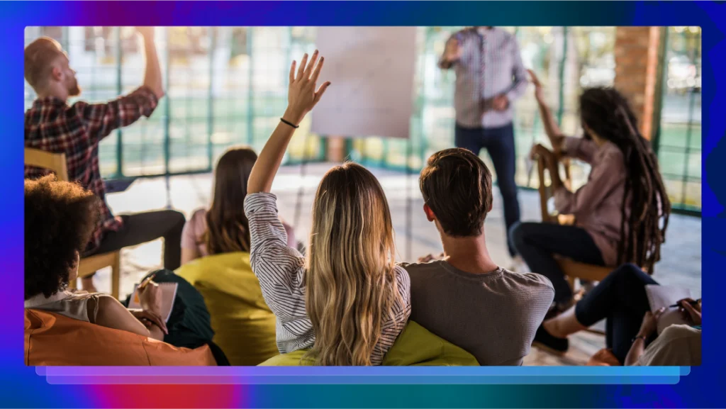 A group of people participating in a focus group in a room with many windows, a few people have their hands raised.