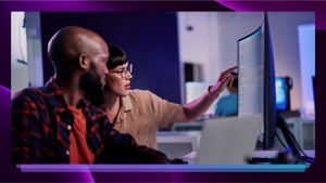 Woman pointing at a computer screen and showing it to her colleague, who is looking up from his laptop.