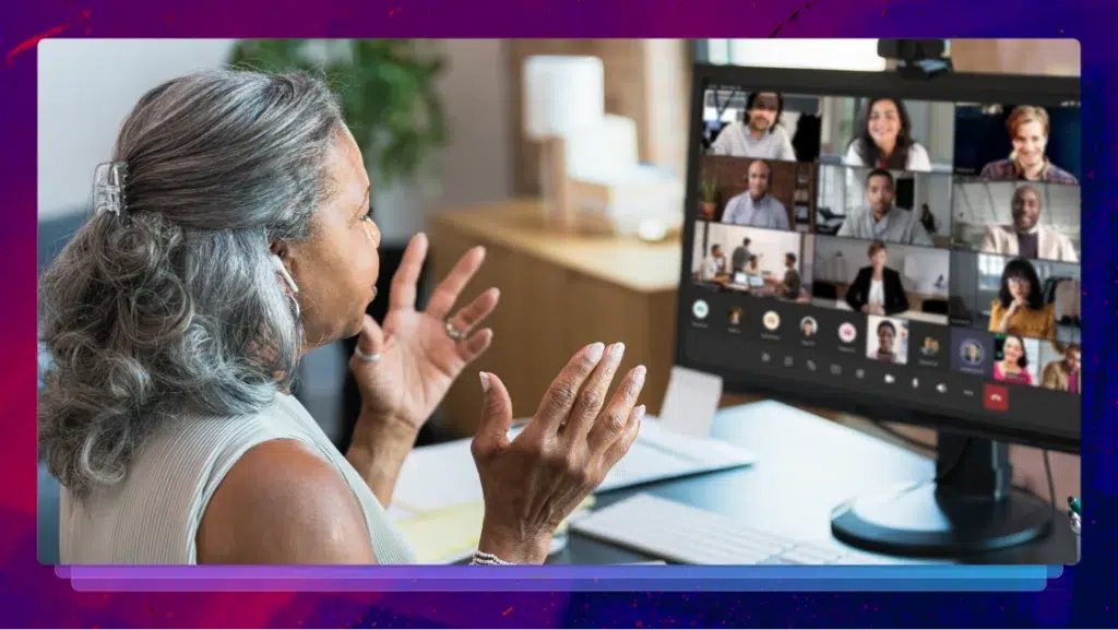 A woman sitting at a desk while engaging in the Microsoft teams meeting on her monitor.