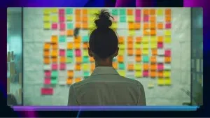 A person stands facing a wall covered with colorful sticky notes, appearing to be focused on the notes. The scene evokes a sense of brainstorming.