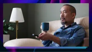 A man on a couch with a mug and remote in his hand.
