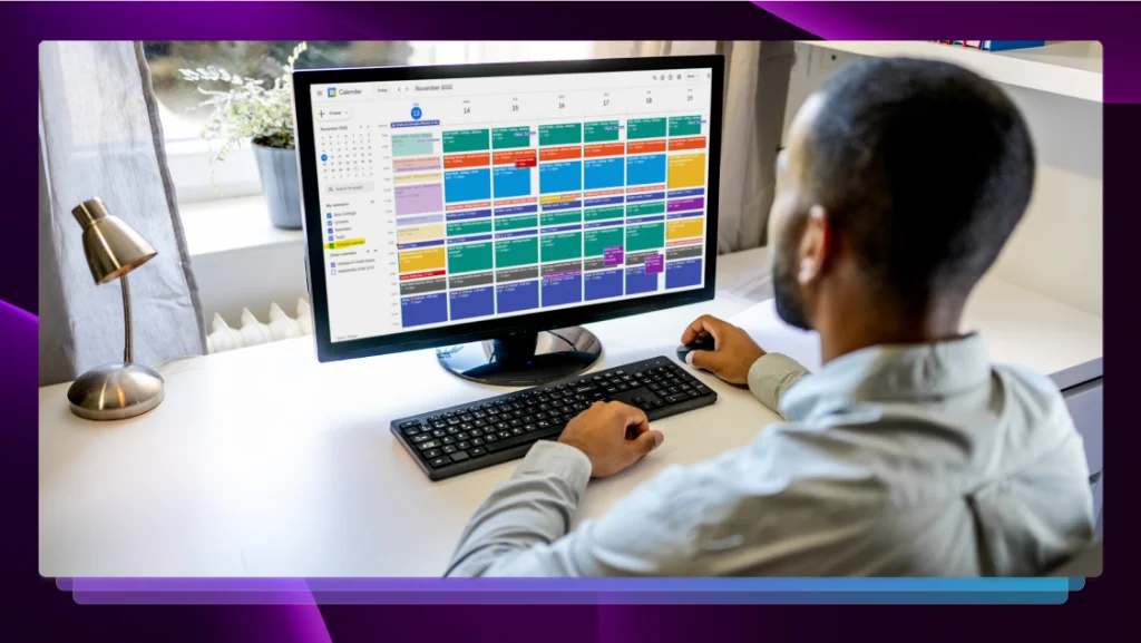 A man sitting at a desk and managing his fully booked calendar on a widescreen monitor.